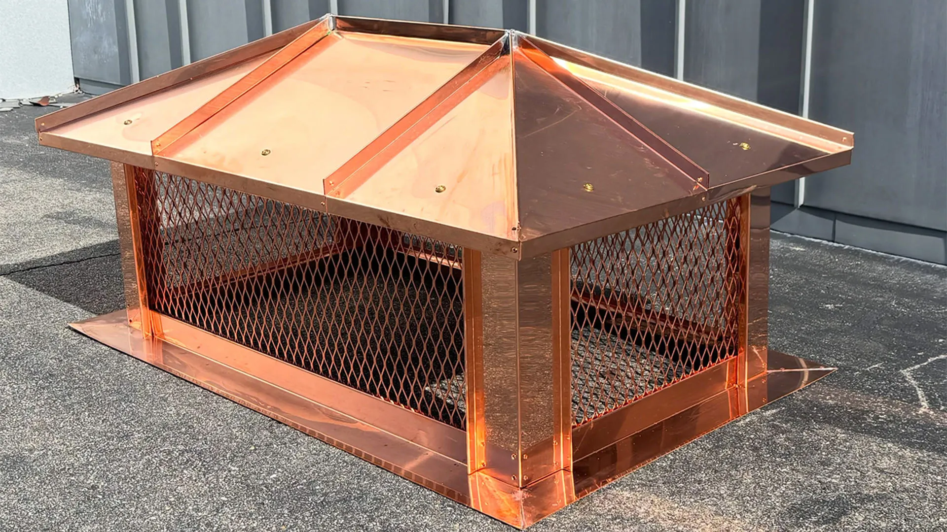 Copper top-mount chimney cap with a hip-and-ridge standing-seam roof